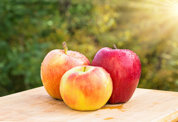 A close-up of three ripe apples sitting on an outdoor table.