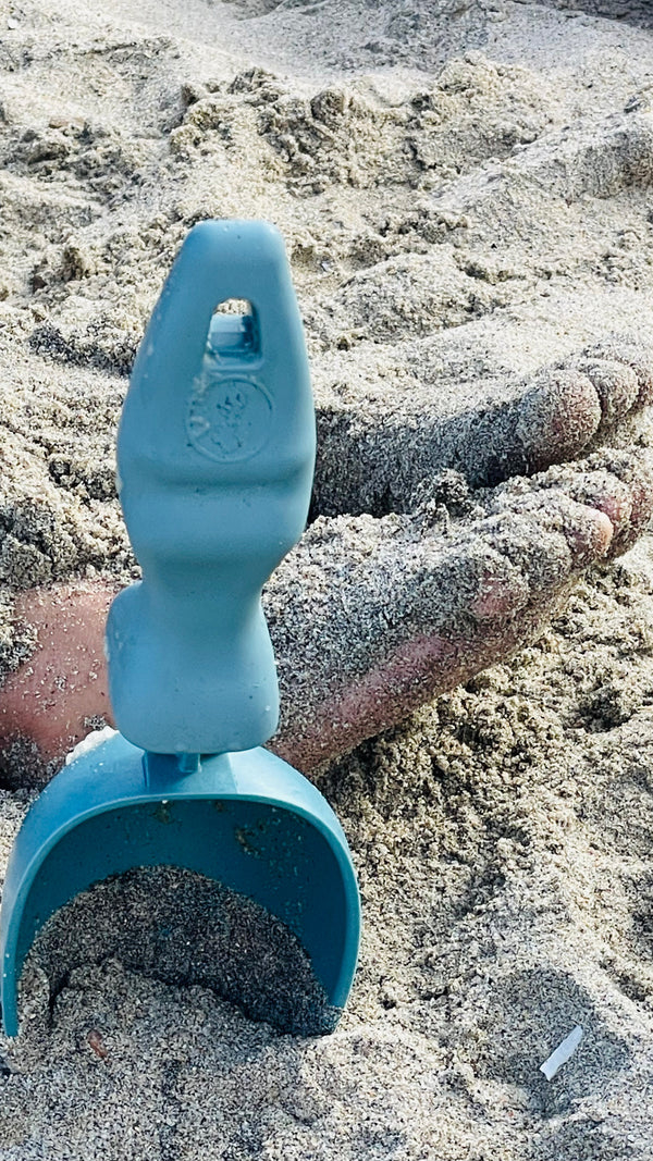 In the foreground is a Rutabaga Garden School stuck into the sand. In the background are the sandy feet of a child.