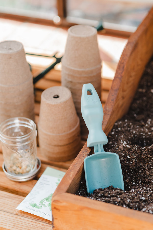 A Rutabaga Garden Tool trowel in some seed starting soil next to brown compostable seed starting pots.
