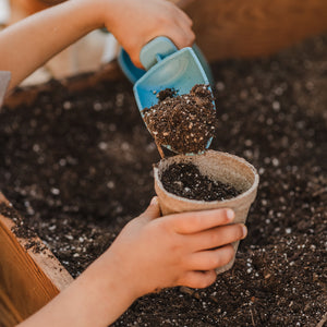 A picture of a child's hands as they use the Rutabaga Garden Tool trowel to fill a seedling pot with seed startng soil.