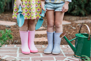 The legs of two young kids wearing summer clothing and rain boots while holding a Rutabaga garden scoop and Rutabaga garden trowel.
