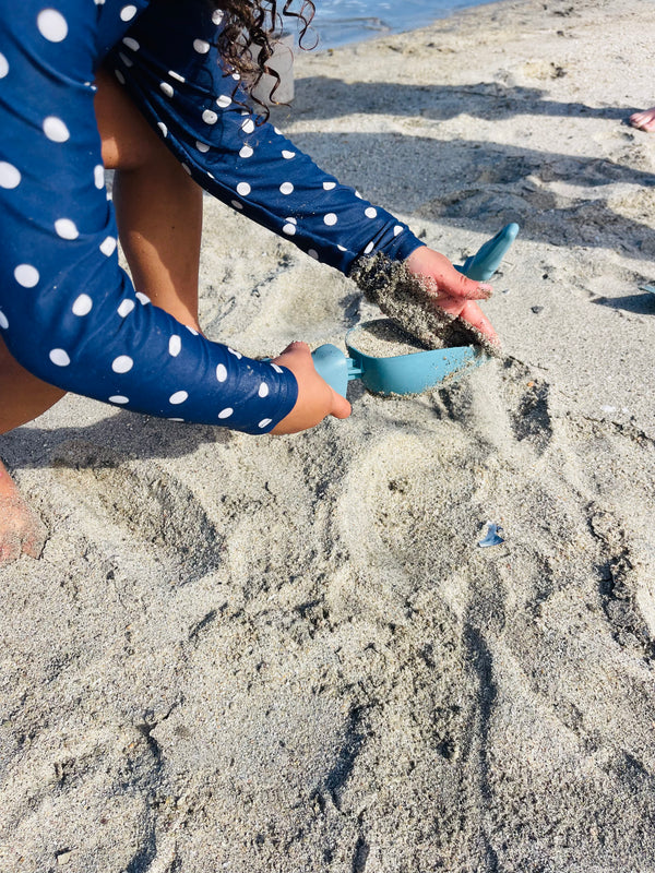 A child scooping beach sand into her Rutabaga Garden Tool scoop.