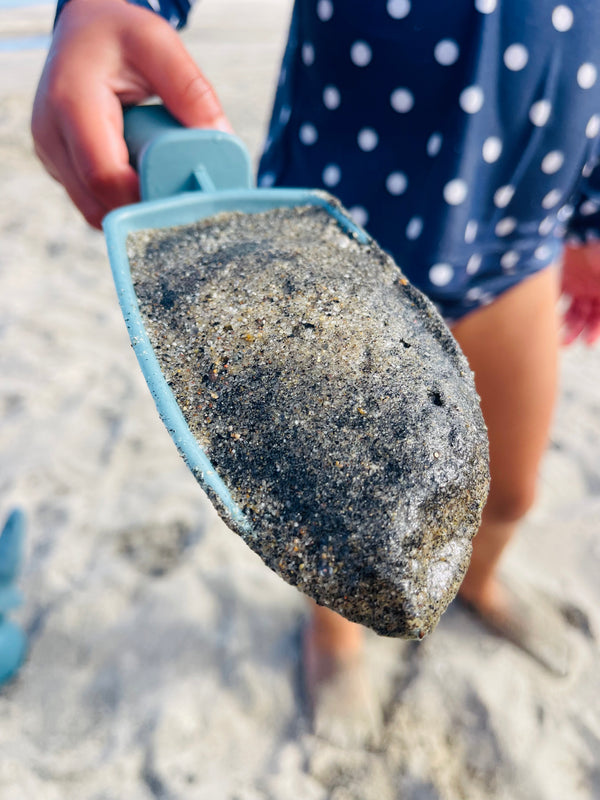A young girl in a polka dot blue and white swimsuit with a close up on the Rutabaga Garden Tool trowel that is filled with sand.