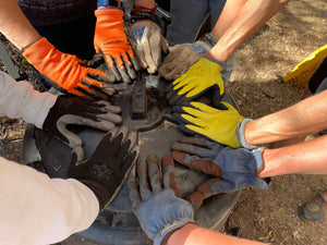 Five pair of hand with garden gloves who all are placing their hands on the lid of a composter.