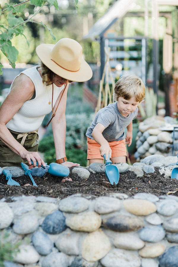 A woman and a young boy digging into a garden bed using the scoop tool.