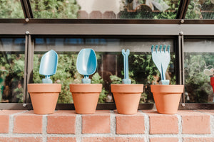 Trowel, scoop, weeder, and rake displayed in flower pots.