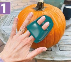A woman's hand showing how the Pumpkin Scraper tool fits on two fingers.