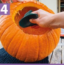 A woman's hand using the Pumpkin Scraper tool to clean out the inside of a pumpkin.